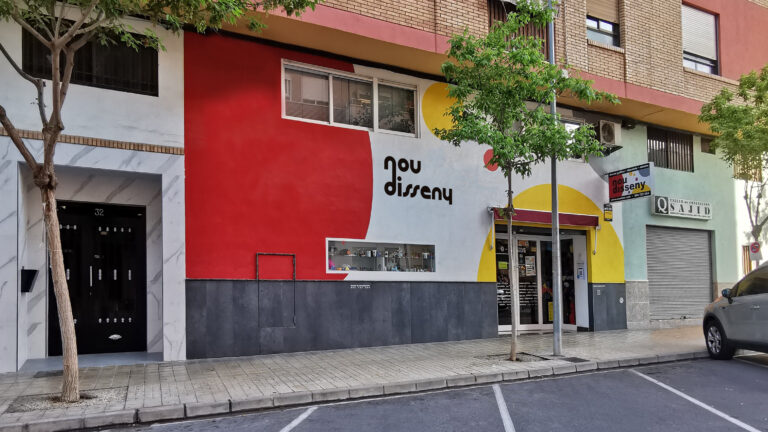 Colorful building mural with the words 'nou disseny' and a storefront below on a tree-lined street.